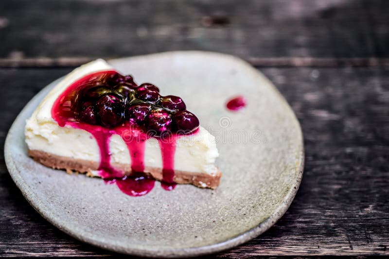 Cheesecake z czarną jagodą na wierzchołku i syropie który nalewali w kafelkowego talerz umieszczał na drewnianym stole fotografia stock