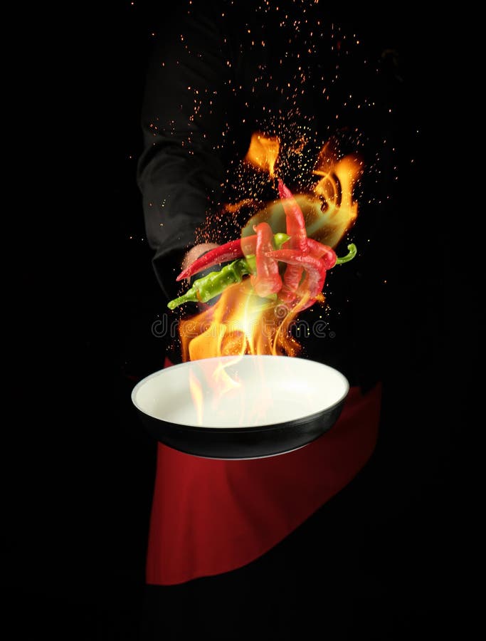 Chef in a black uniform holds a round pan and throws up red and green whole chili peppers