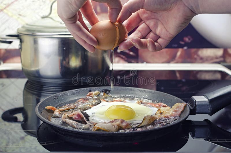 Chef breaks egg into frying pan, cooks bacon and fried eggs in frying  pan, cooks in kitchen, close up front view