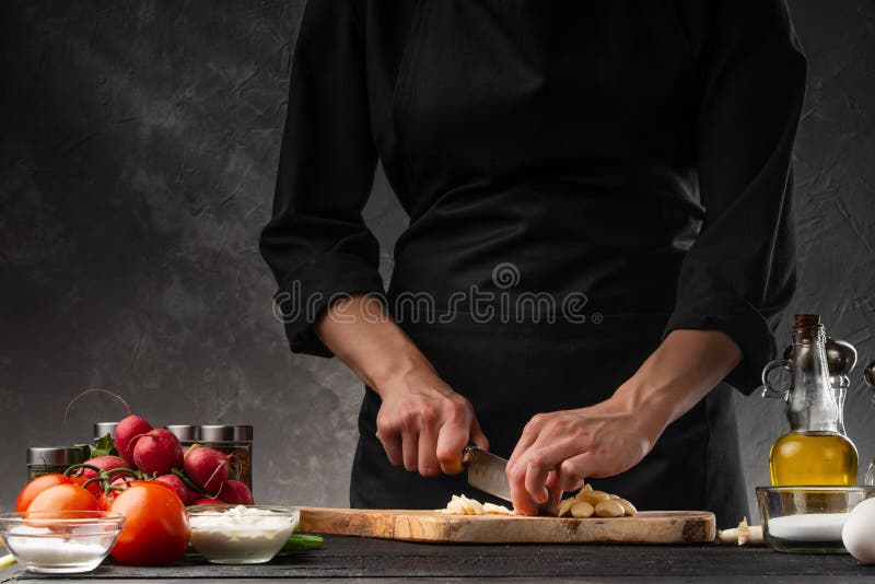 Chef chopping garlic for cooking. Against the background of a gray wall, and vegetables. Cooking and recipe book