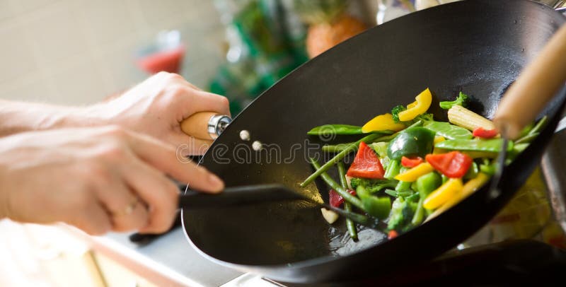 Kuchař vaření zeleniny ve wok pánvi.