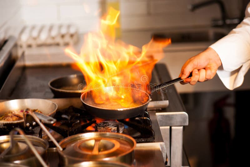 Cocinero cocinando fuego en fritura sartén sobre el La cocina cocina.