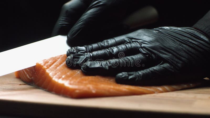 Chef en gros plan avec le morceau de saumons rouges Le chef professionnel dans les gants noirs tient le morceau de saumoné frais