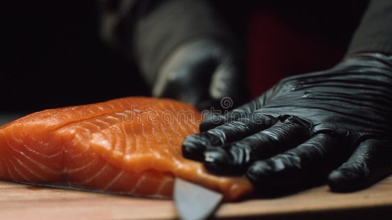 Chef en gros plan avec le morceau de saumons rouges Chef professionnel dans le morceau noir de coupes de gants de saumons frais d