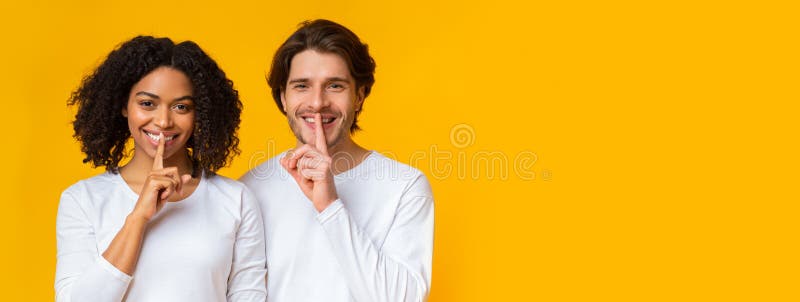 Do not speak. Portrait of cheerful interracial couple showing silence sign, holding fingers on lips, posing together over yellow background. Do not speak. Portrait of cheerful interracial couple showing silence sign, holding fingers on lips, posing together over yellow background