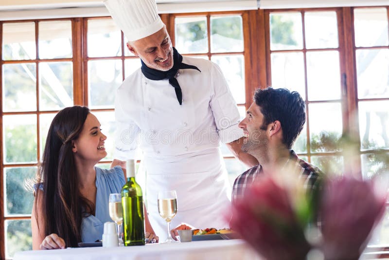 Chef-kok die aan paar bij restaurant spreken royalty-vrije stock foto Chef-kok die aan paar bij restaurant spreken royalty-vrije stock foto