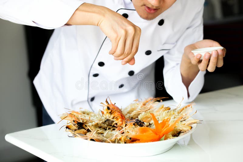 Chef-kok die zoute overal geroosterde garnalen in de keuken bestrooien stock foto's Chef-kok die zoute overal geroosterde garnalen in de keuken bestrooien stock foto's