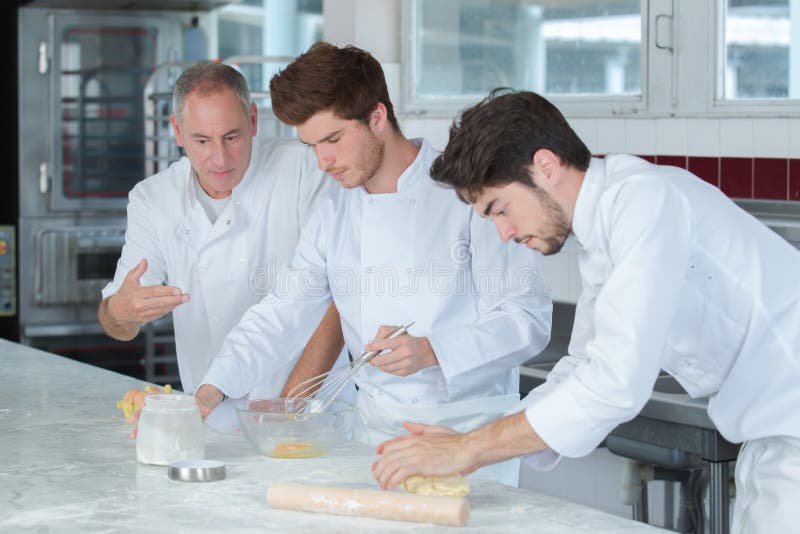 Chef-kok en stagiairs in restaurantkeuken royalty-vrije stock afbeeldingen Chef-kok en stagiairs in restaurantkeuken royalty-vrije stock afbeeldingen
