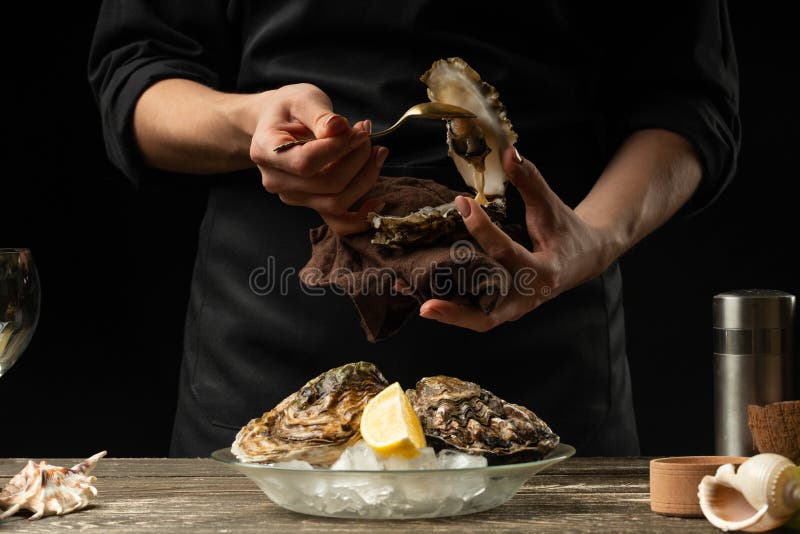 The chef opens and cleans the raw oyster against a background of white wine, lettuce, lemons and limes