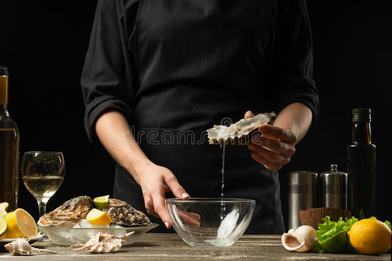 The chef opens and cleans the raw oyster against a background of white wine, lettuce, lemons and limes