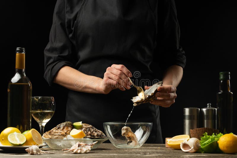 The chef opens and cleans the raw oyster against a background of white wine, lettuce, lemons and limes