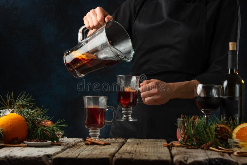 Chef pours aromatic muled wine with fragrant spices into glasses on rustic table with festive composition background. Concept of