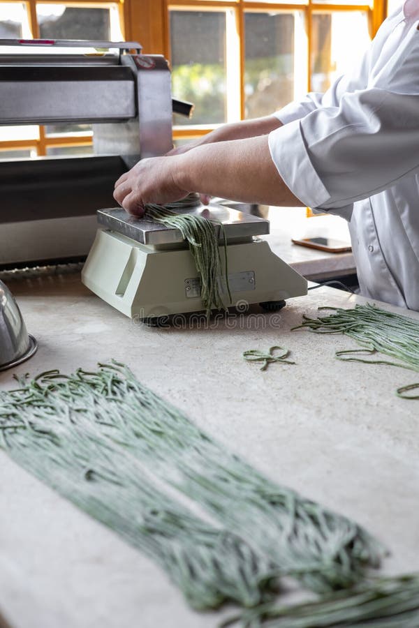 Chef Prepares Green Noodles Using a Pasta Machine in a Trendy Kitchen