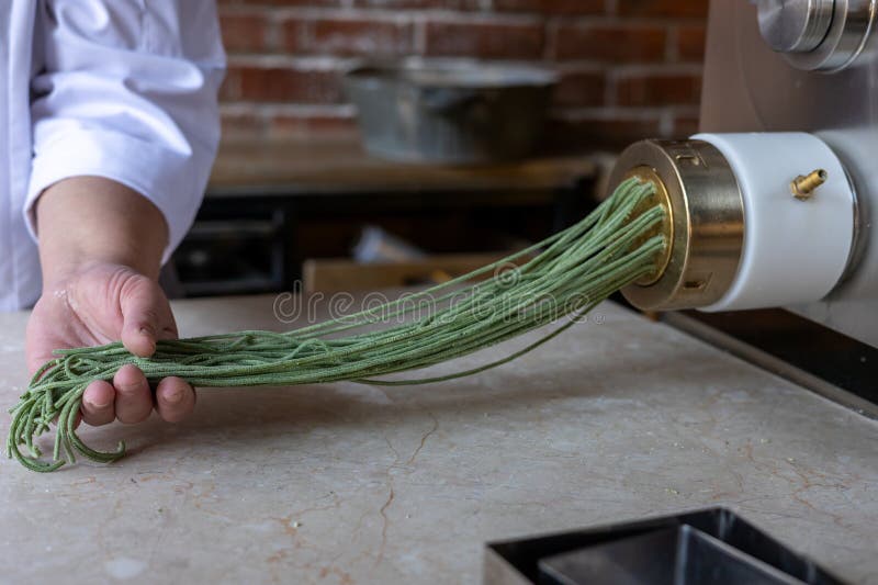 Chef Prepares Green Noodles Using a Pasta Machine in a Trendy Kitchen