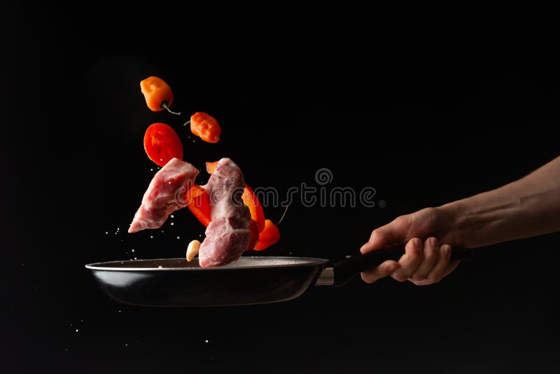 Chef prepares meat with vegetables, on a black background, roasting, tasty food, recipe book, menu, restaurant business