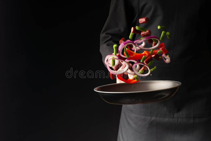 Chef preparing pepperoni sausages with green beans, sweet bell peppers and red onion rings, on a black background, a recipe book