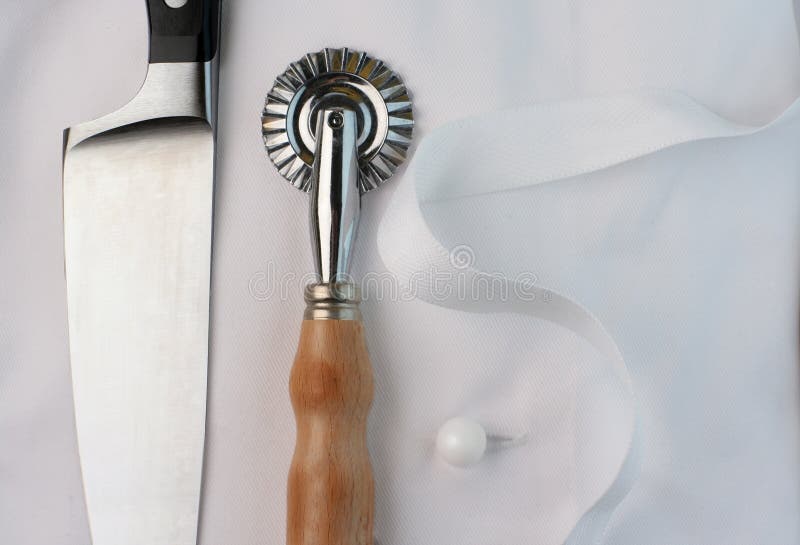 Wide cropped view of a pasta or ravioli wheel cutter, cook's knife and chef's uniform. Wide cropped view of a pasta or ravioli wheel cutter, cook's knife and chef's uniform.