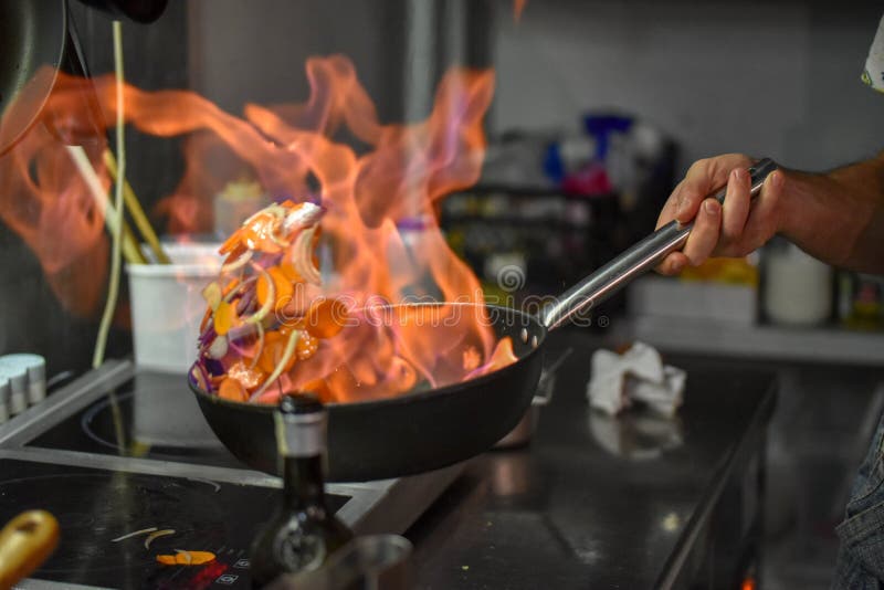 Chef tossing vegetables flambe in a pan over the burner royalty free stock photo Chef tossing vegetables flambe in a pan over the burner royalty free stock photo