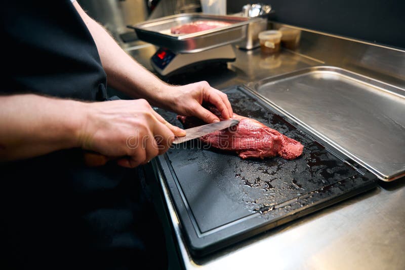 Chef varón parcial cortando filete de carne con cuchillo en el tablero de compras en la mesa fotografía de archivo libre de regalías