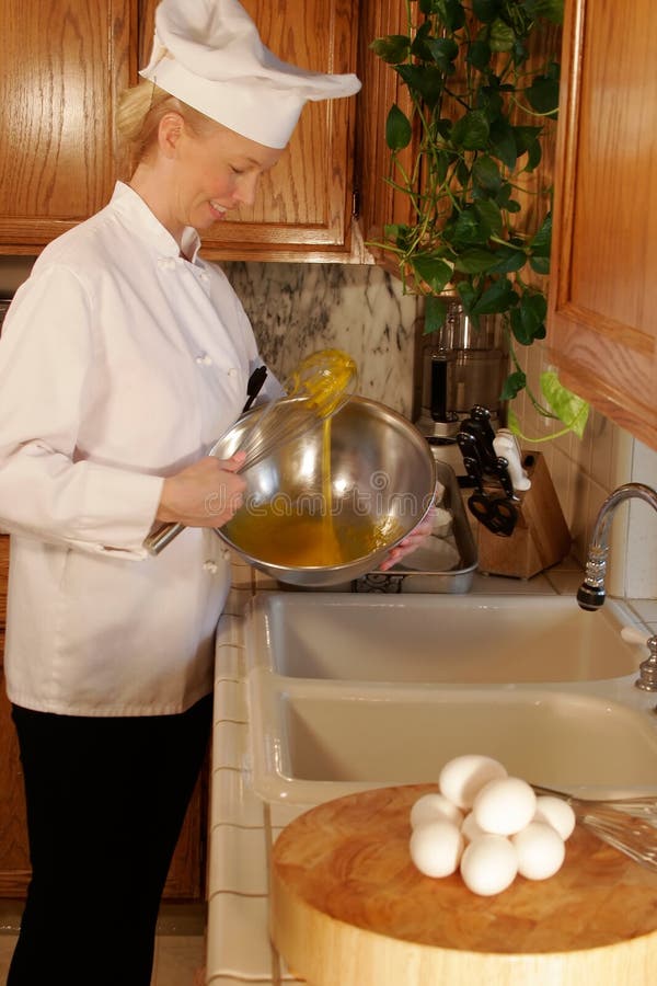 Female Cheef whisking eggs in a stainless bowl, in the kitchen. Female Cheef whisking eggs in a stainless bowl, in the kitchen.
