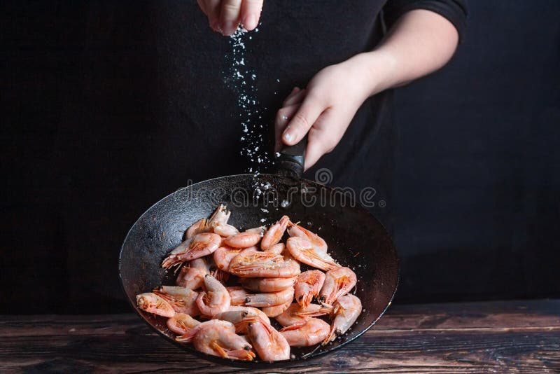 Chef at work. Hand holds a hot pan with fried shrimp and salt the food