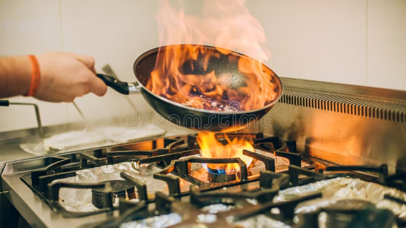 Chef cook prepares a meal in the frying pan with flame fire burn in the kitchen in the restaurant. Chef cook prepares a meal in the frying pan with flame fire burn in the kitchen in the restaurant