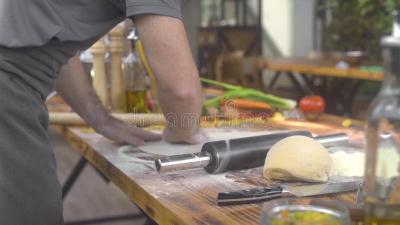 Chefkoch, der Mehl auf Pizzateig beim Rollen mit Zylindermutter besprüht Mann, der Teig für frische Teigwaren auf italienisch mac