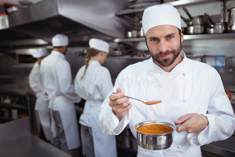 Chefprobierenlebensmittel vom Löffel in der Küche am Restaurant stockfotografie Chefprobierenlebensmittel vom Löffel in der Küche am Restaurant stockfotografie