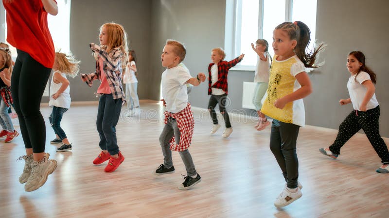 Group of little boys and girls dancing while having choreography class in the dance studio. Female dance teacher and children. Contemp dance. Hip hop. Kids and sport. Full length. Group of little boys and girls dancing while having choreography class in the dance studio. Female dance teacher and children. Contemp dance. Hip hop. Kids and sport. Full length