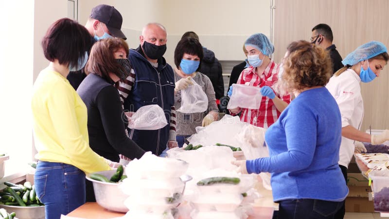 Cherkasy ukraine maio 2020 : voluntários embrulham lancheiras com refeições caritativas em sacos plásticos adicionam pepinos. alim