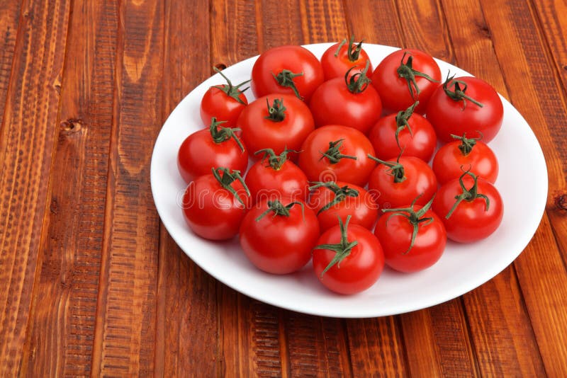 Cherry tomatoes on white plate on wooden background