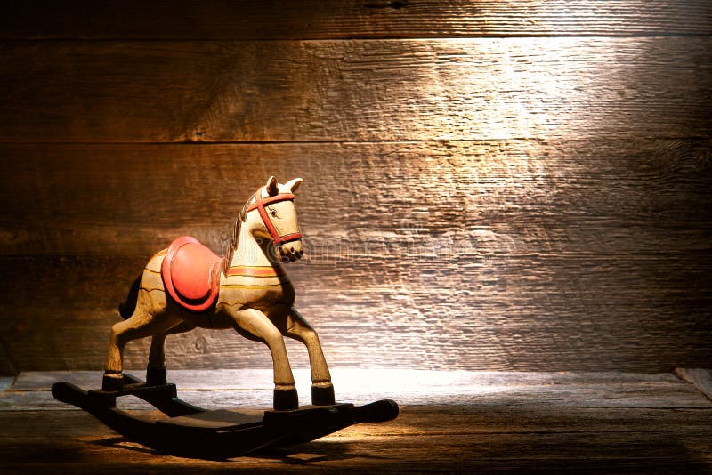 Nostalgic Americana scene of an antique reproduction wood toy rocking horse on aged wooden plank floor in a dusty old house attic lit by soft diffused sunlight through a window. Nostalgic Americana scene of an antique reproduction wood toy rocking horse on aged wooden plank floor in a dusty old house attic lit by soft diffused sunlight through a window