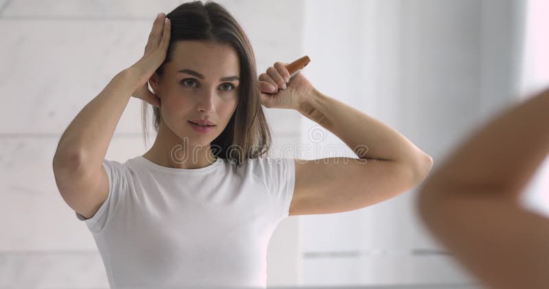 Cheveux de brossage de sourire de jeune femme regardant à travers le miroir banque de vidéos