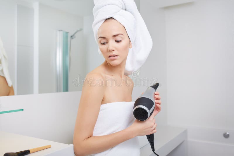 Cheveux séchants de jeune femme dans la salle de bains photo stock Cheveux séchants de jeune femme dans la salle de bains photo stock