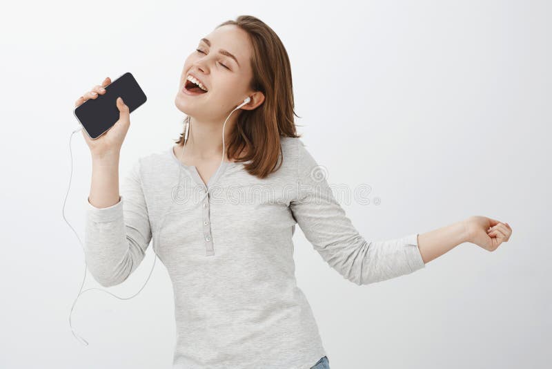 Chi ha bisogno del karaoke quando lo smartphone esiste ragazza affascinante felice con brevi capelli marroni che assomigliano al immagini stock Chi ha bisogno del karaoke quando lo smartphone esiste ragazza affascinante felice con brevi capelli marroni che assomigliano al immagini stock