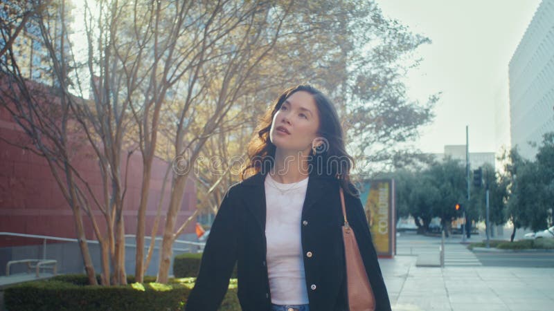 Chica caminante sonriendo a la luz del sol en la calle. brunette asiática disfrutando del paisaje urbano.