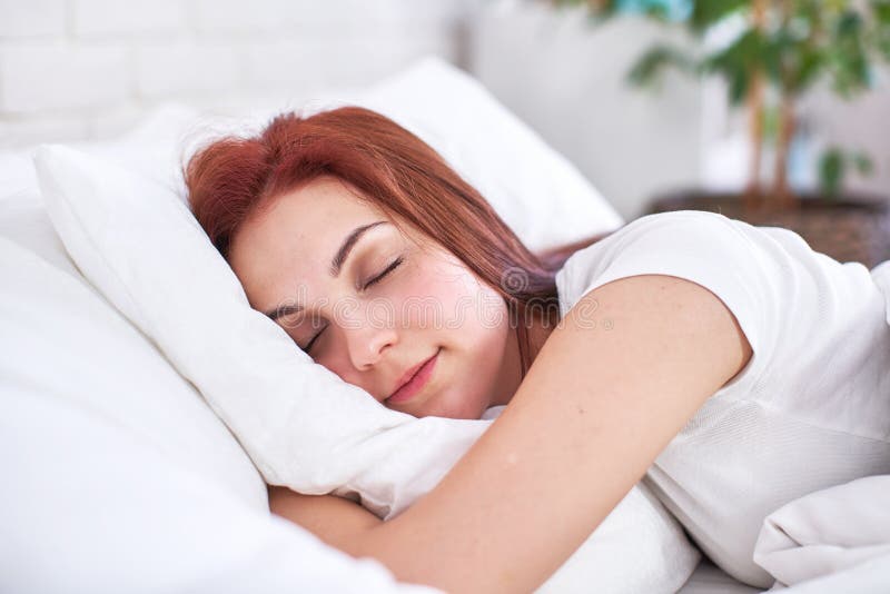 Chica hermosa de cabello rojo duerme abrazando una almohada en una cama clara en el dormitorio dulce chica durmiendo dormitorio e imagen de archivo libre de regalías Chica hermosa de cabello rojo duerme abrazando una almohada en una cama clara en el dormitorio dulce chica durmiendo dormitorio e imagen de archivo libre de regalías