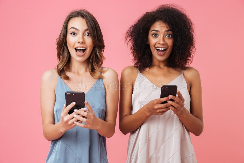 Chica joven alegre dos en los vestidos que sostienen los teléfonos móviles fotografía de archivo Chica joven alegre dos en los vestidos que sostienen los teléfonos móviles fotografía de archivo