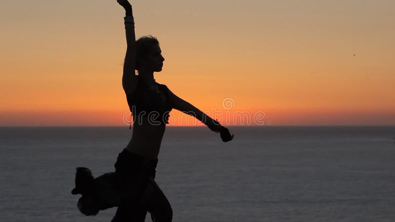 Chica joven bonita que baila danza oriental en la puesta del sol