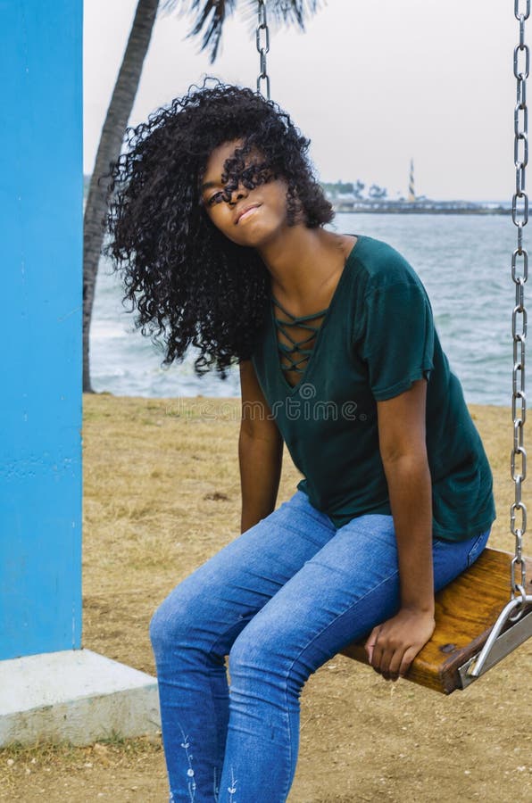 Chica joven del color negro, pelo de risa en la noria, sentándose disfrutando de un día de verano foto de archivo libre de regalías Chica joven del color negro, pelo de risa en la noria, sentándose disfrutando de un día de verano foto de archivo libre de regalías