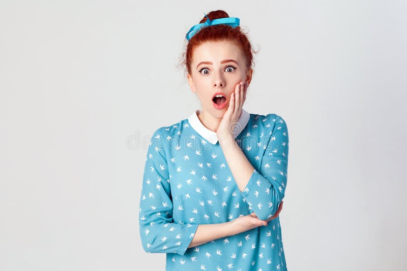 Ginger young girl screaming with shock, holding hands on her cheeks. Isolated studio shot on gray background. Ginger young girl screaming with shock, holding hands on her cheeks. Isolated studio shot on gray background.