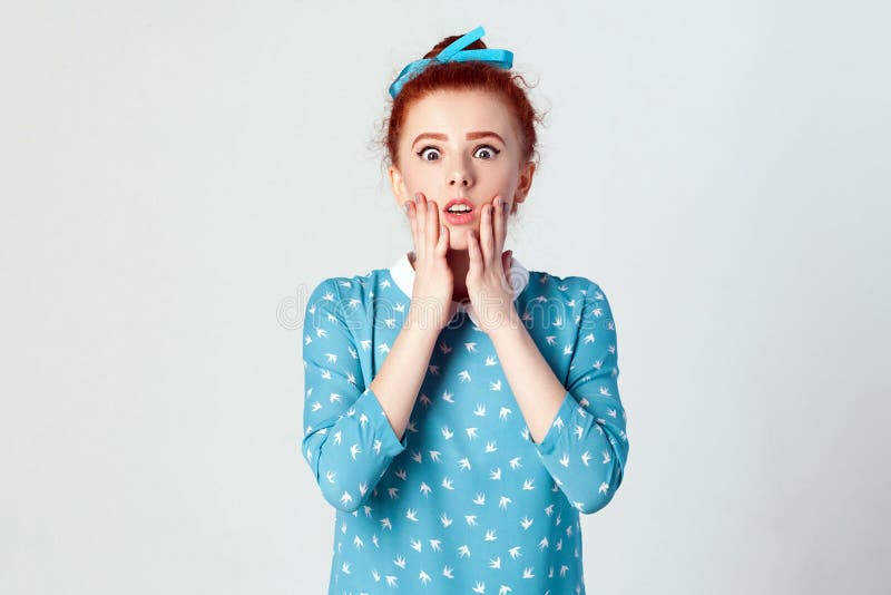 Human face expressions and emotions. Redhead young girl touching her cheeks and looking at camera with shocked face. studio shot on gray background. Human face expressions and emotions. Redhead young girl touching her cheeks and looking at camera with shocked face. studio shot on gray background.