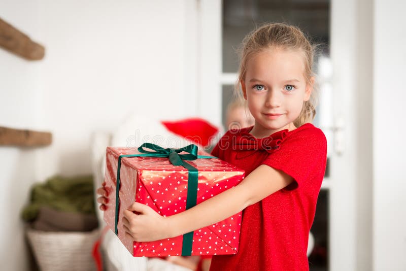 Chica joven emocionada linda que lleva a cabo el regalo de Navidad grande, sonriendo y mirando la cámara Niño feliz en la Navidad fotos de archivo Chica joven emocionada linda que lleva a cabo el regalo de Navidad grande, sonriendo y mirando la cámara Niño feliz en la Navidad fotos de archivo