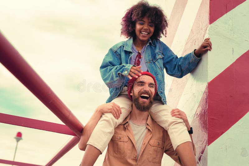 Chica joven emocionada que se sienta en los hombros de su novio y sonrisa confiables imagenes de archivo Chica joven emocionada que se sienta en los hombros de su novio y sonrisa confiables imagenes de archivo