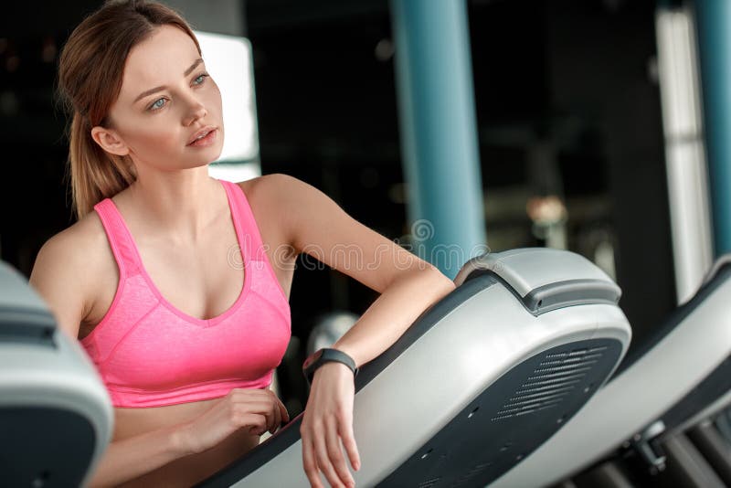 Chica joven en la forma de vida sana del gimnasio que se inclina en la rueda de ardilla que mira hacia fuera la ventana pensativa fotografía de archivo Chica joven en la forma de vida sana del gimnasio que se inclina en la rueda de ardilla que mira hacia fuera la ventana pensativa fotografía de archivo