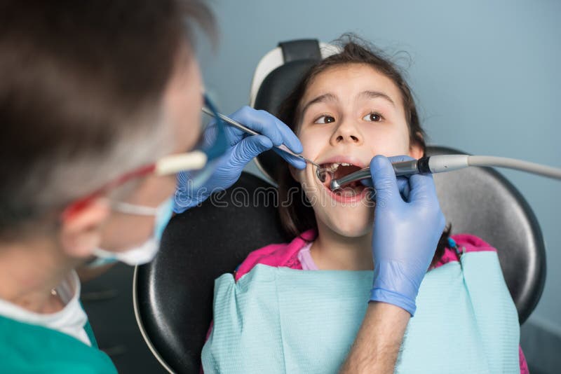 Chica joven en la visita dental Dentista pediátrico mayor que trata los dientes pacientes de la muchacha en la oficina dental fotos de archivo libres de regalías Chica joven en la visita dental Dentista pediátrico mayor que trata los dientes pacientes de la muchacha en la oficina dental fotos de archivo libres de regalías