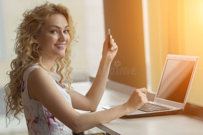 Chica joven en un vestido con la tarjeta de crédito a disposición que sonríe y que mira la cámara imagen de archivo libre de regalías Chica joven en un vestido con la tarjeta de crédito a disposición que sonríe y que mira la cámara imagen de archivo libre de regalías