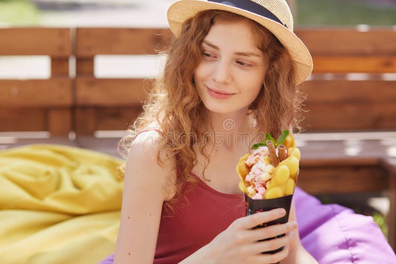 Chica joven hermosa adorable blanda que mira a un lado, pasando tiempo solamente afuera, sosteniendo el postre en ambas manos, so imagenes de archivo Chica joven hermosa adorable blanda que mira a un lado, pasando tiempo solamente afuera, sosteniendo el postre en ambas manos, so imagenes de archivo