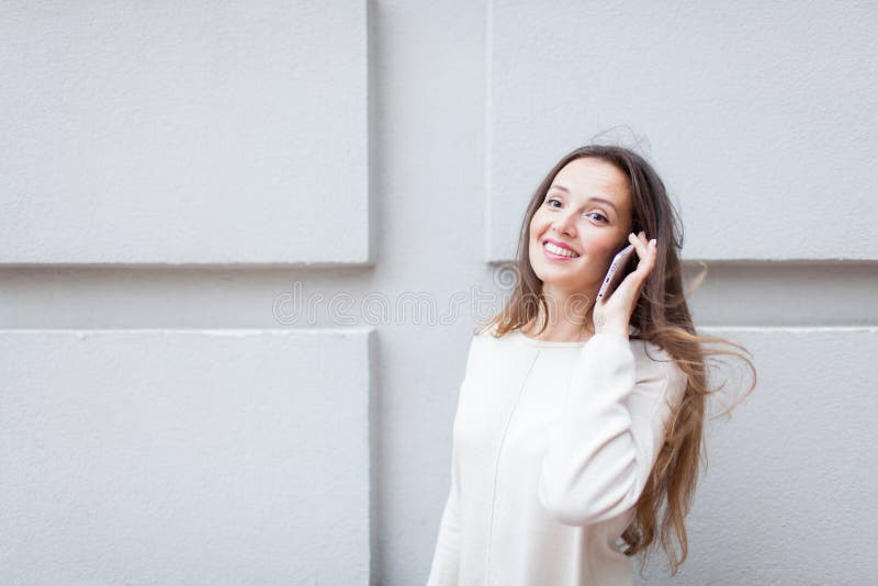 Chica joven hermosa con el pelo marrón largo parado mientras que monta la vespa, para llamar a un amigo en el teléfono en el fond foto de archivo libre de regalías Chica joven hermosa con el pelo marrón largo parado mientras que monta la vespa, para llamar a un amigo en el teléfono en el fond foto de archivo libre de regalías