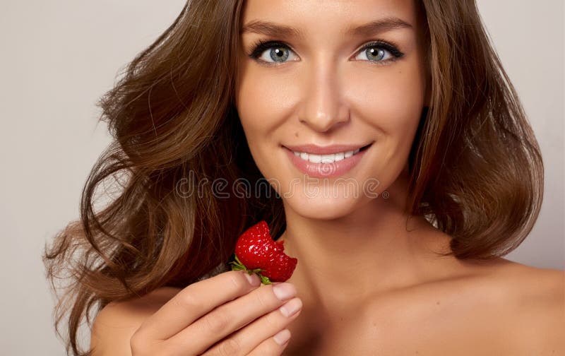 Chica joven hermosa con los dientes blancos rectos que sonríe y que come las fresas fotos de archivo Chica joven hermosa con los dientes blancos rectos que sonríe y que come las fresas fotos de archivo